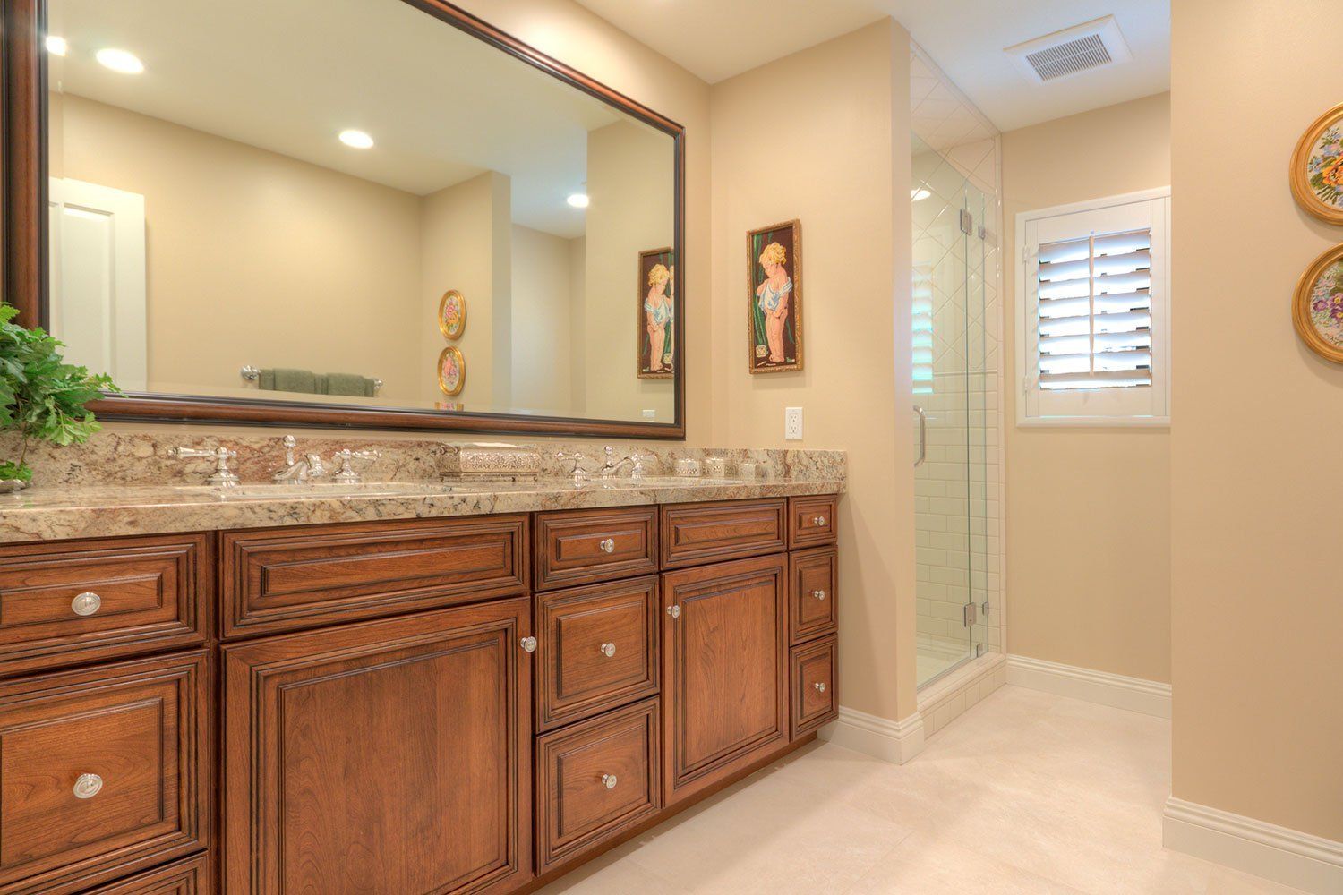 Spacious beige bathroom with double granite vanity, wood cabinets, mirror, and walk-in shower.