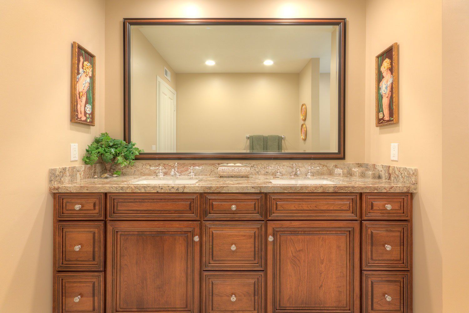 Bathroom vanity with large mirror, granite countertop, wood cabinets, and wall sconces