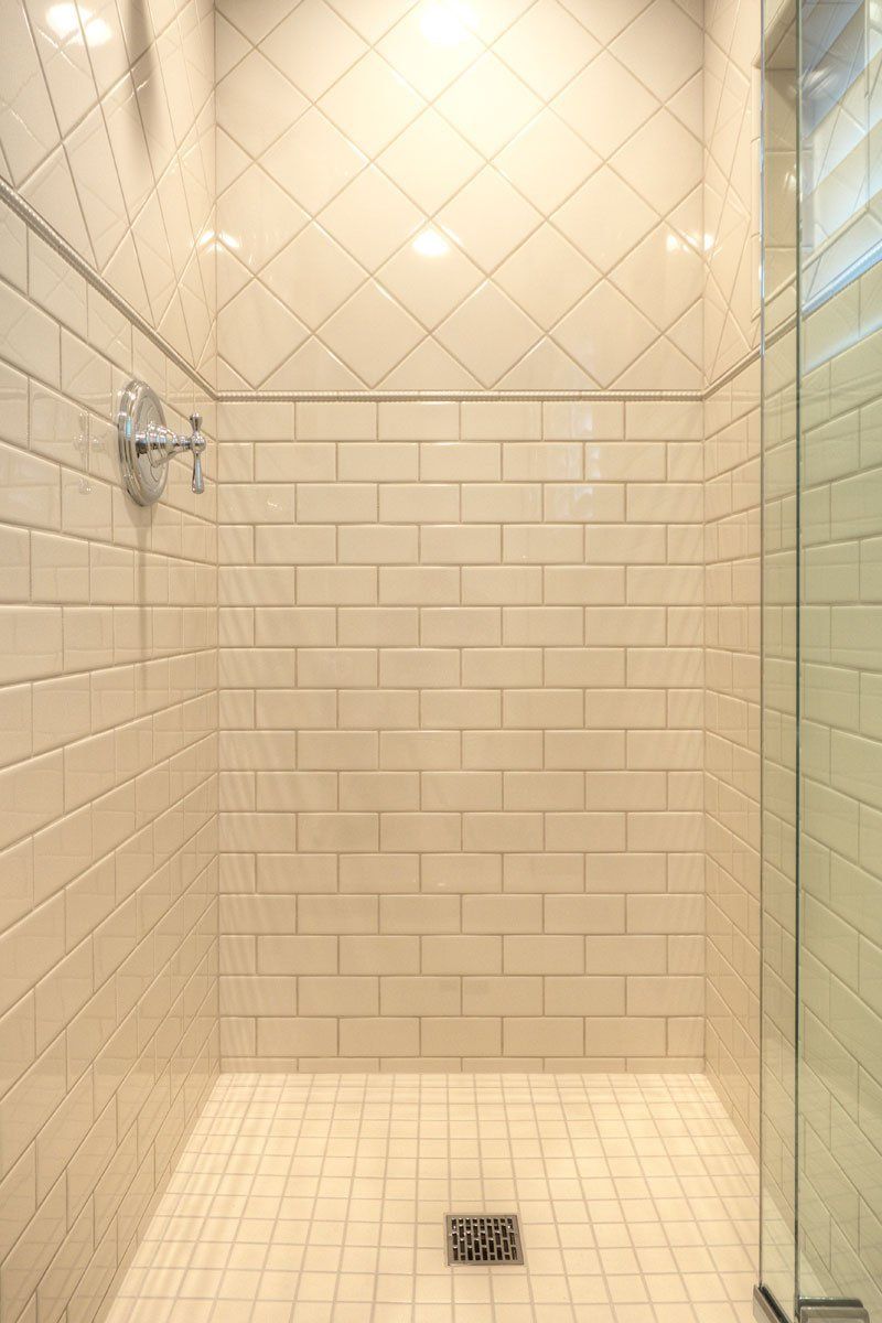 Empty beige tiled shower with glass door and wall-mounted showerhead
