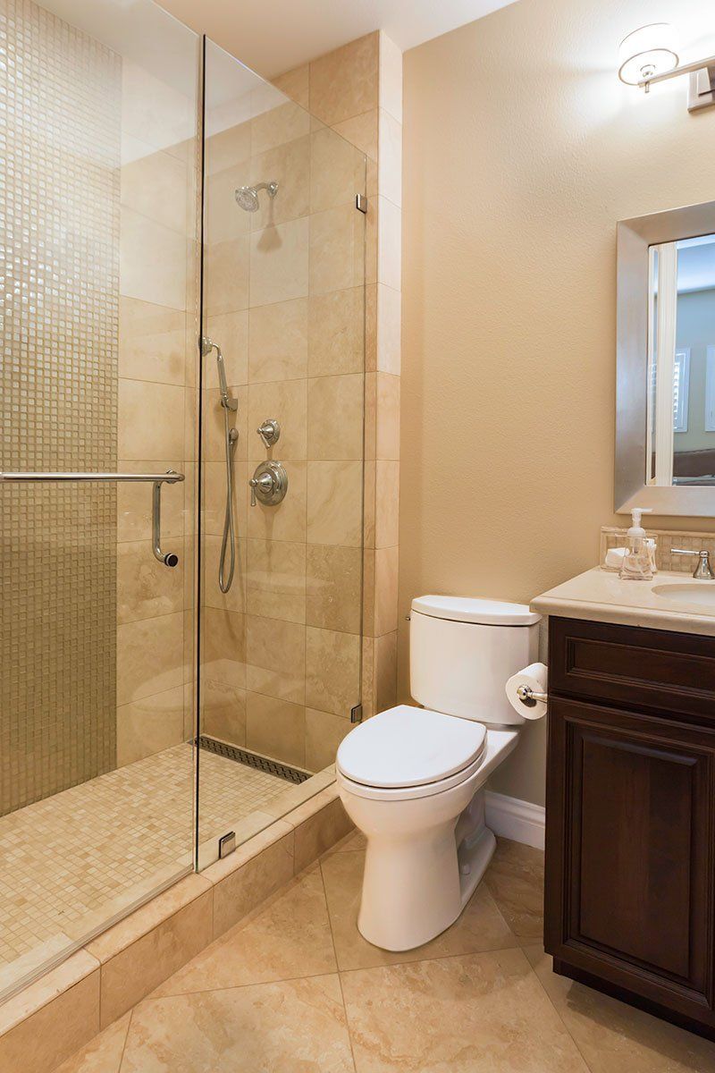 Modern beige bathroom with glass shower, toilet, and dark vanity sink