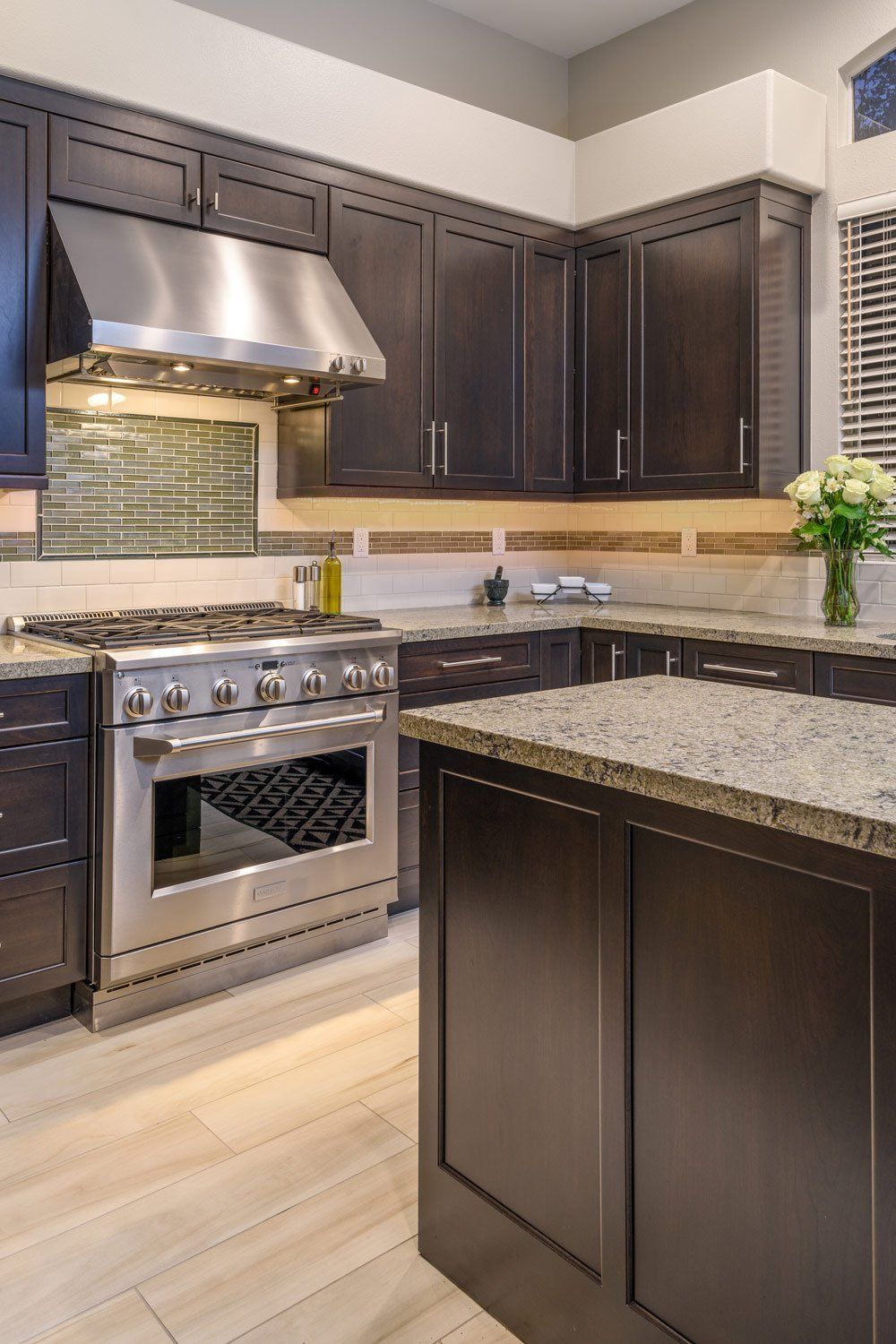 Modern kitchen with dark cabinets, stainless steel stove, granite island, and light wood flooring