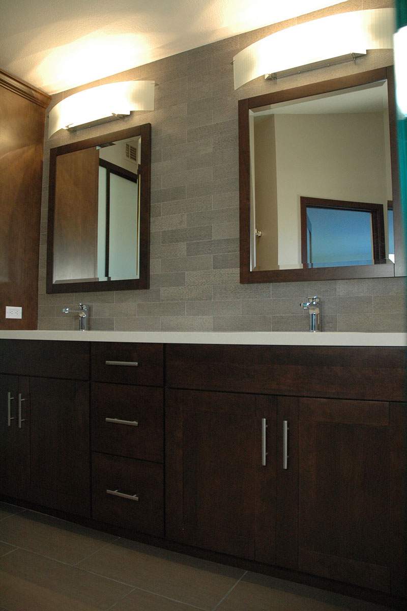 Bathroom vanity with dark wood cabinets, white countertop, and two mirrors above the sinks