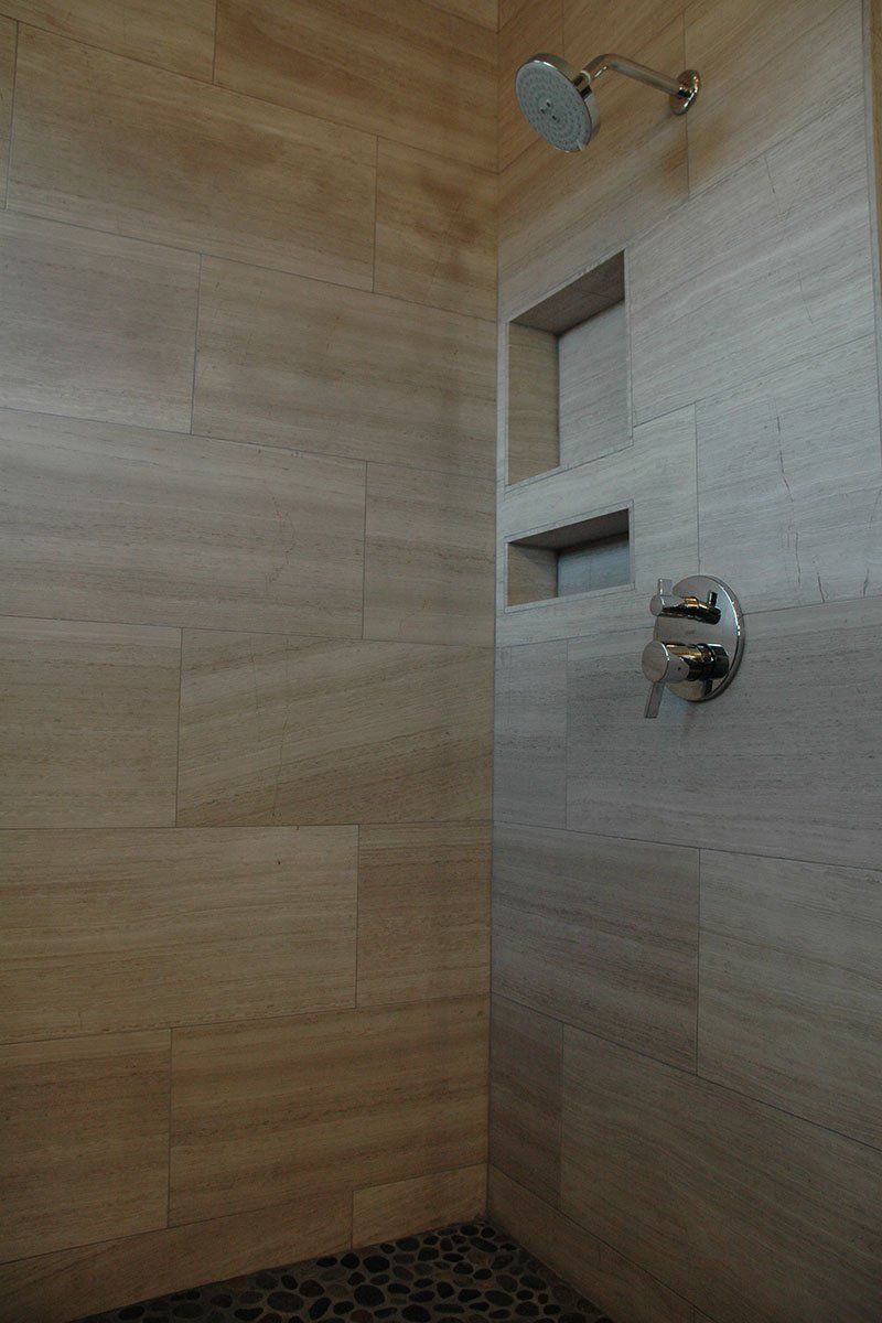 Modern shower with beige tile walls, chrome showerhead, and built-in wall niches
