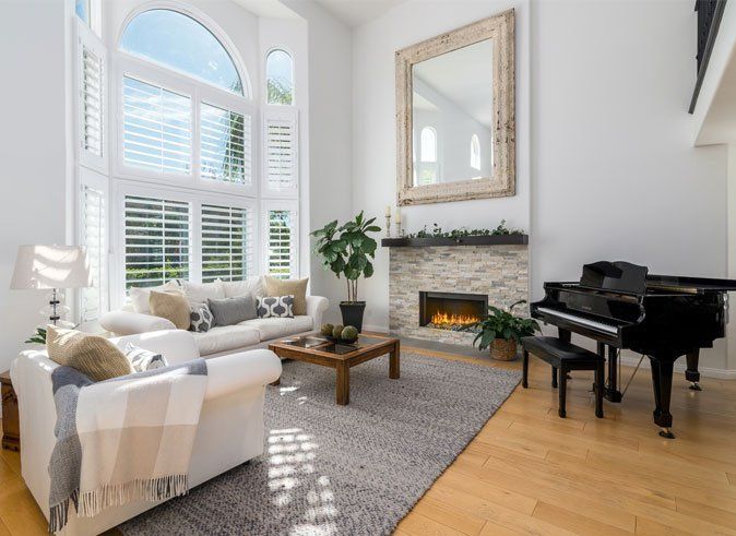 Bright living room with large arched windows, white sofa, fireplace, coffee table, and black grand piano.