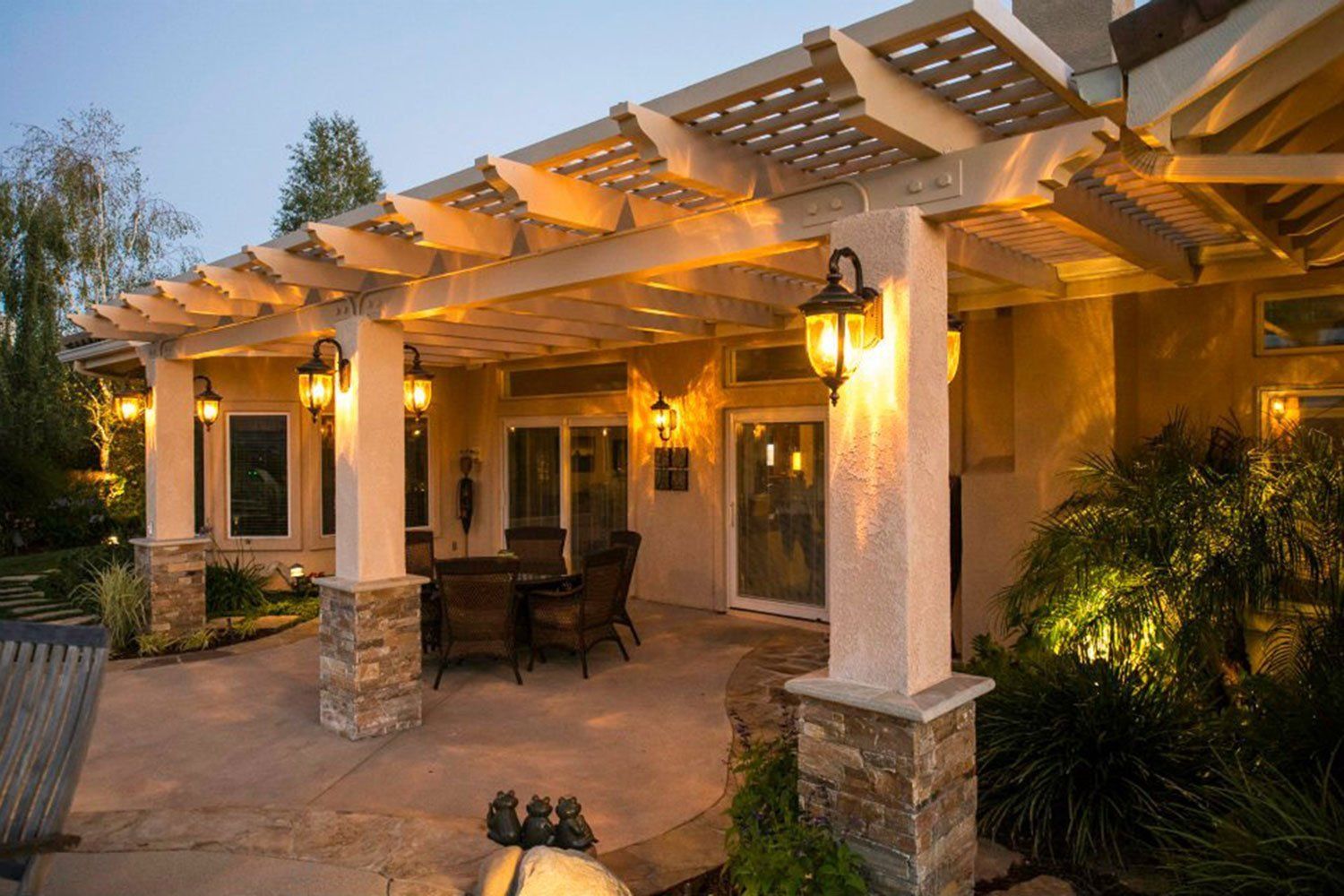 Covered patio with warm lights, stone columns, and outdoor seating at dusk