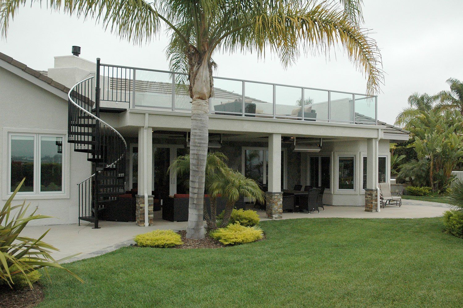 Modern two-story house with a spiral staircase, palm trees, and a green lawn