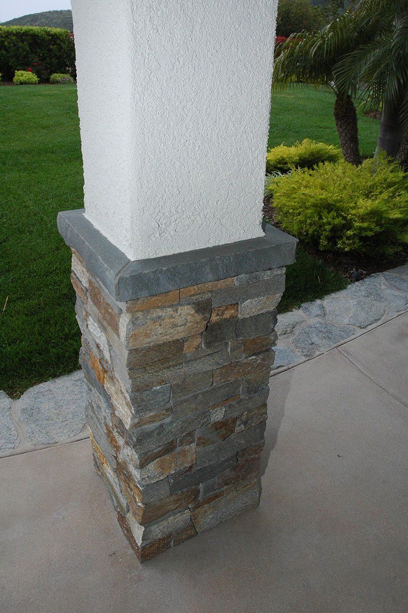Stone-and-white porch column beside a sidewalk and green lawn