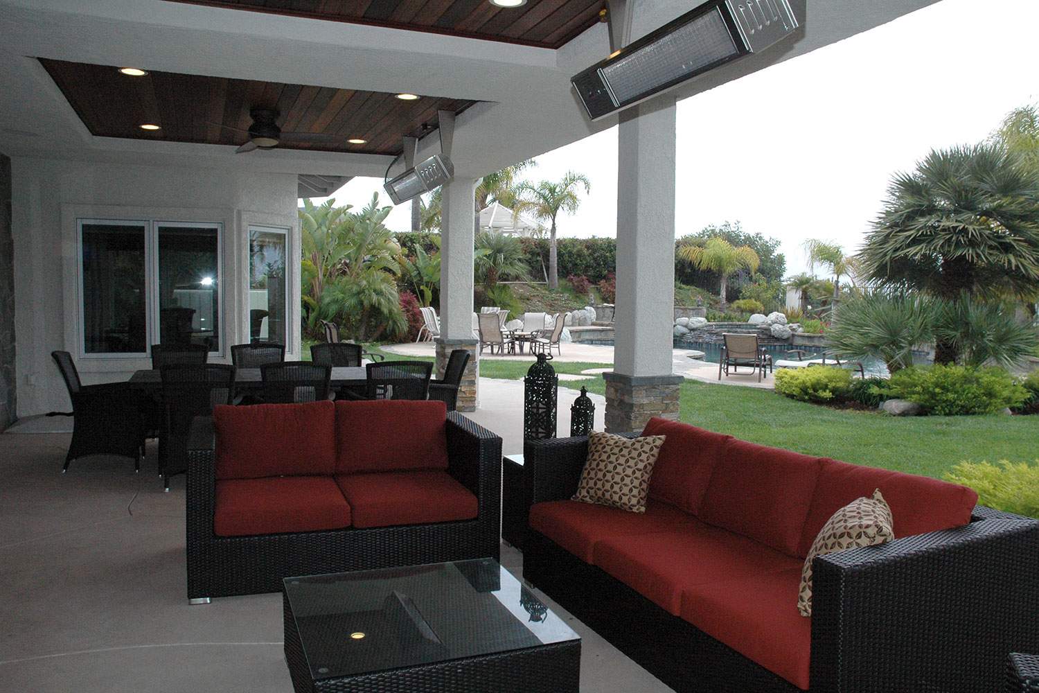 Outdoor patio with red sofas, black chairs, and a view of a garden and pool.
