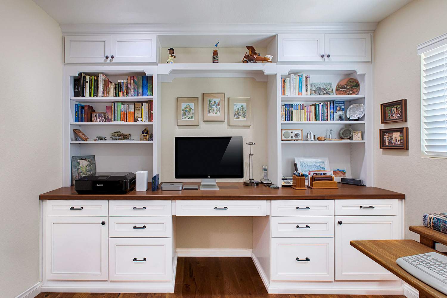 Built-in home office desk with white cabinets, wood top, bookshelves, and a computer monitor