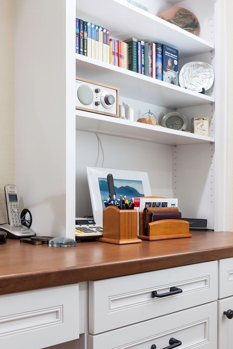 Built-in white bookshelf above wooden desk with books, decor, and a framed photo