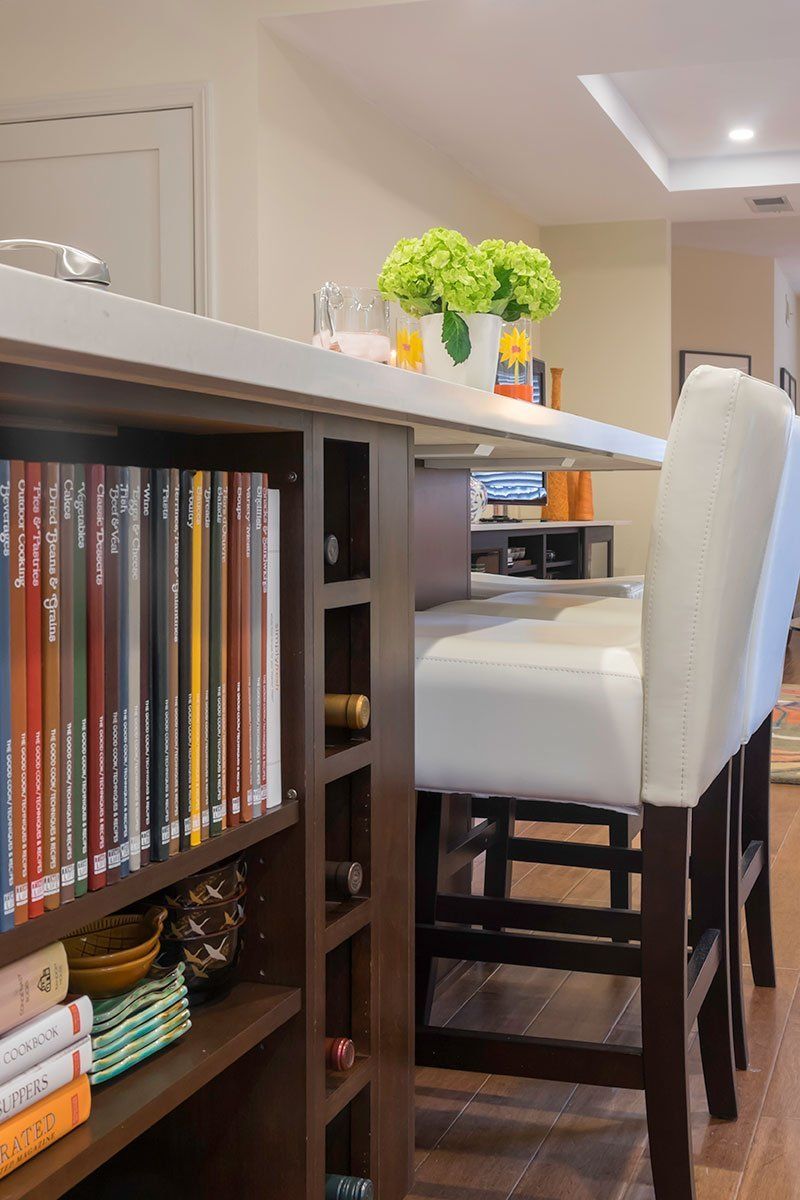 Home bar area with dark wood shelving, white chairs, and a countertop with flowers and candles.