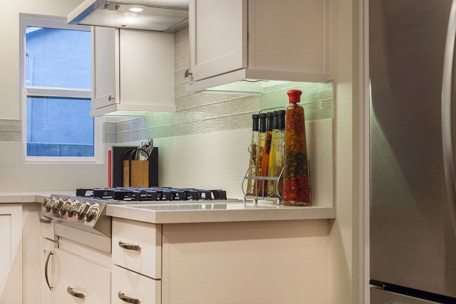Bright kitchen with white cabinets, gas stove, and bottles on the counter beside a window.