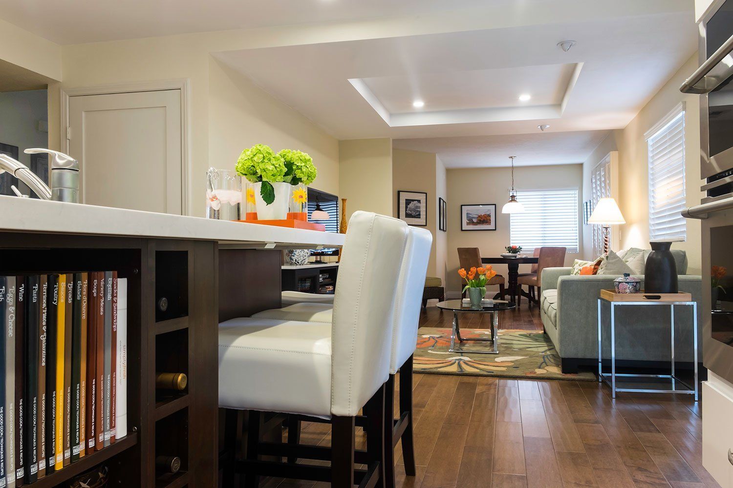 Open-concept dining and living area with wood floors, white chairs, and bright windows