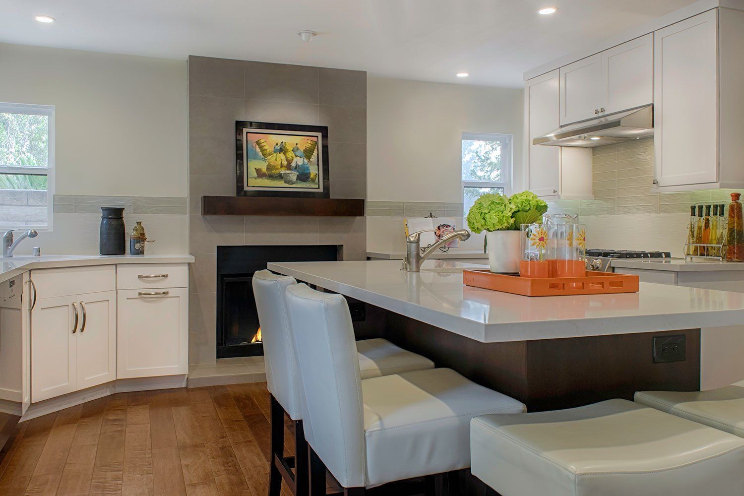 Modern kitchen with white cabinets, island seating, and a fireplace with artwork above it