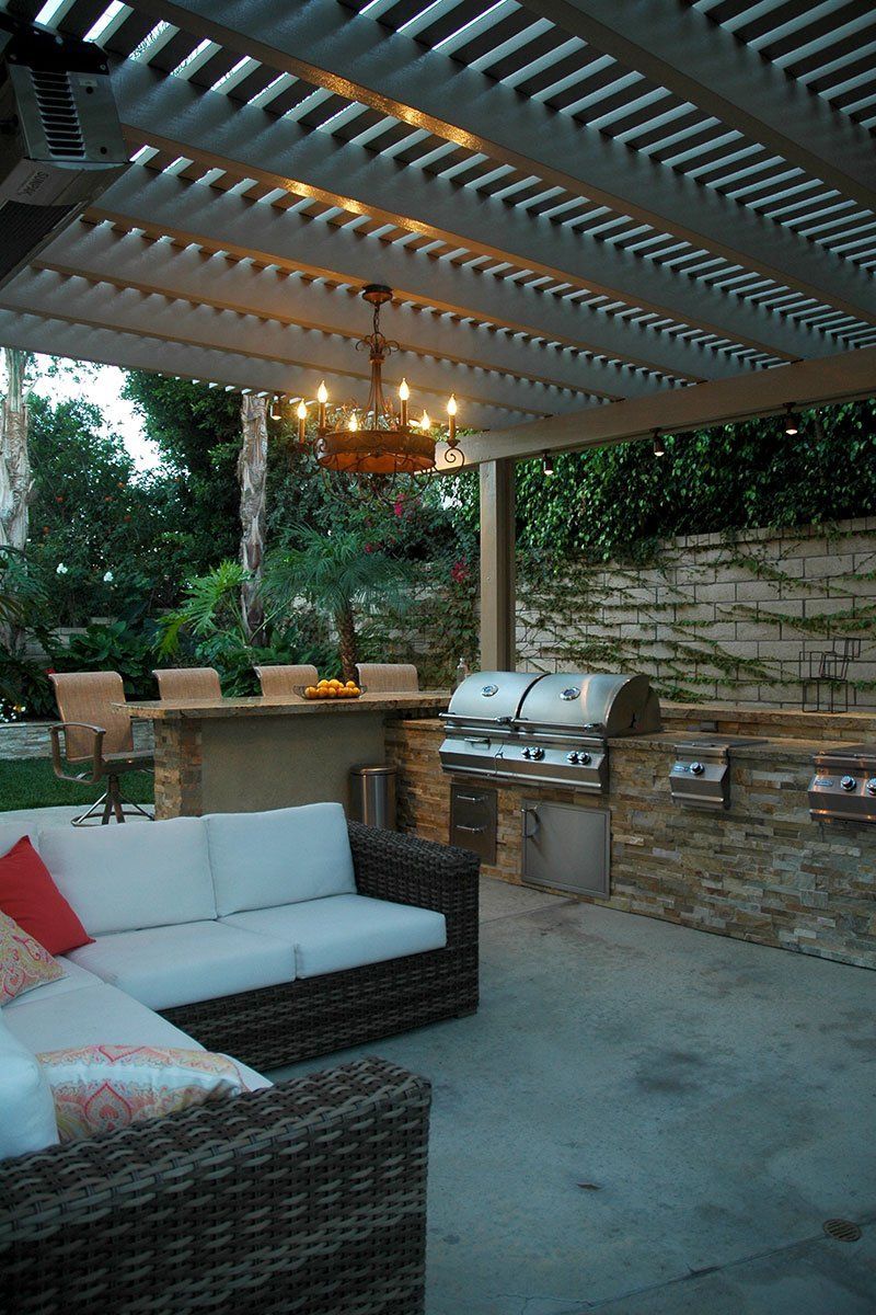 Outdoor patio with wicker seating, chandelier, grill, and pergola at dusk