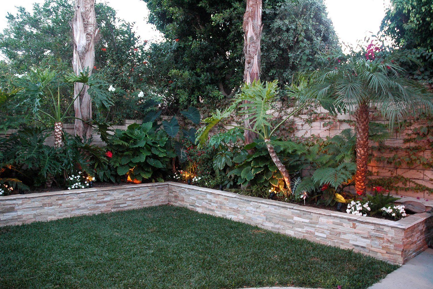 Backyard garden corner with brick planter, lush green plants, and a grass lawn