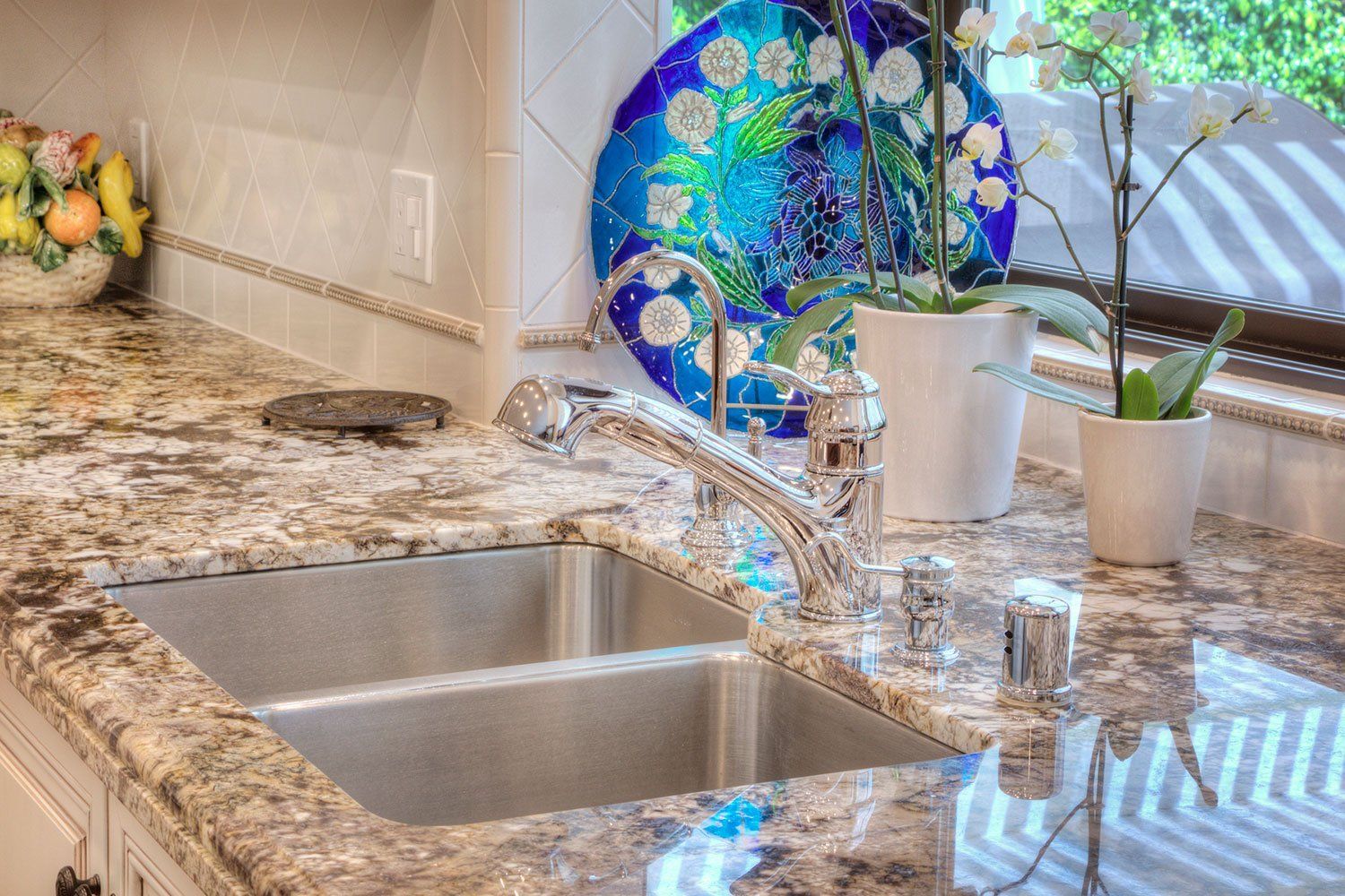 Granite kitchen counter with double sink, chrome faucet, and colorful stained-glass decor by the window