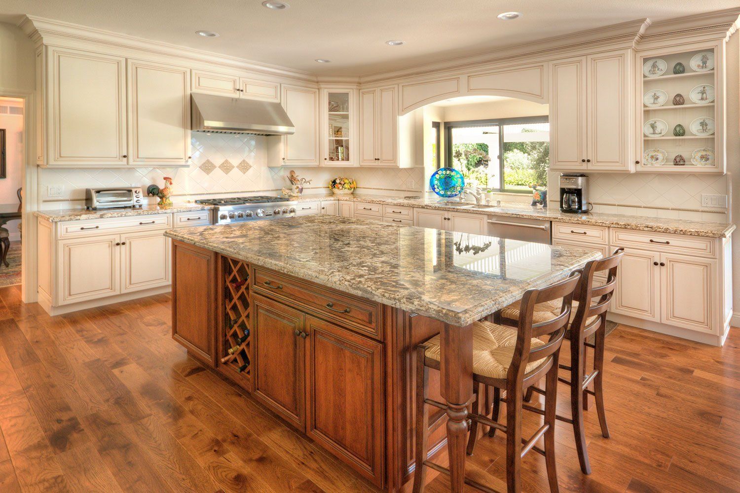 Bright gourmet kitchen with granite island, wood cabinets, and a large window over hardwood floors