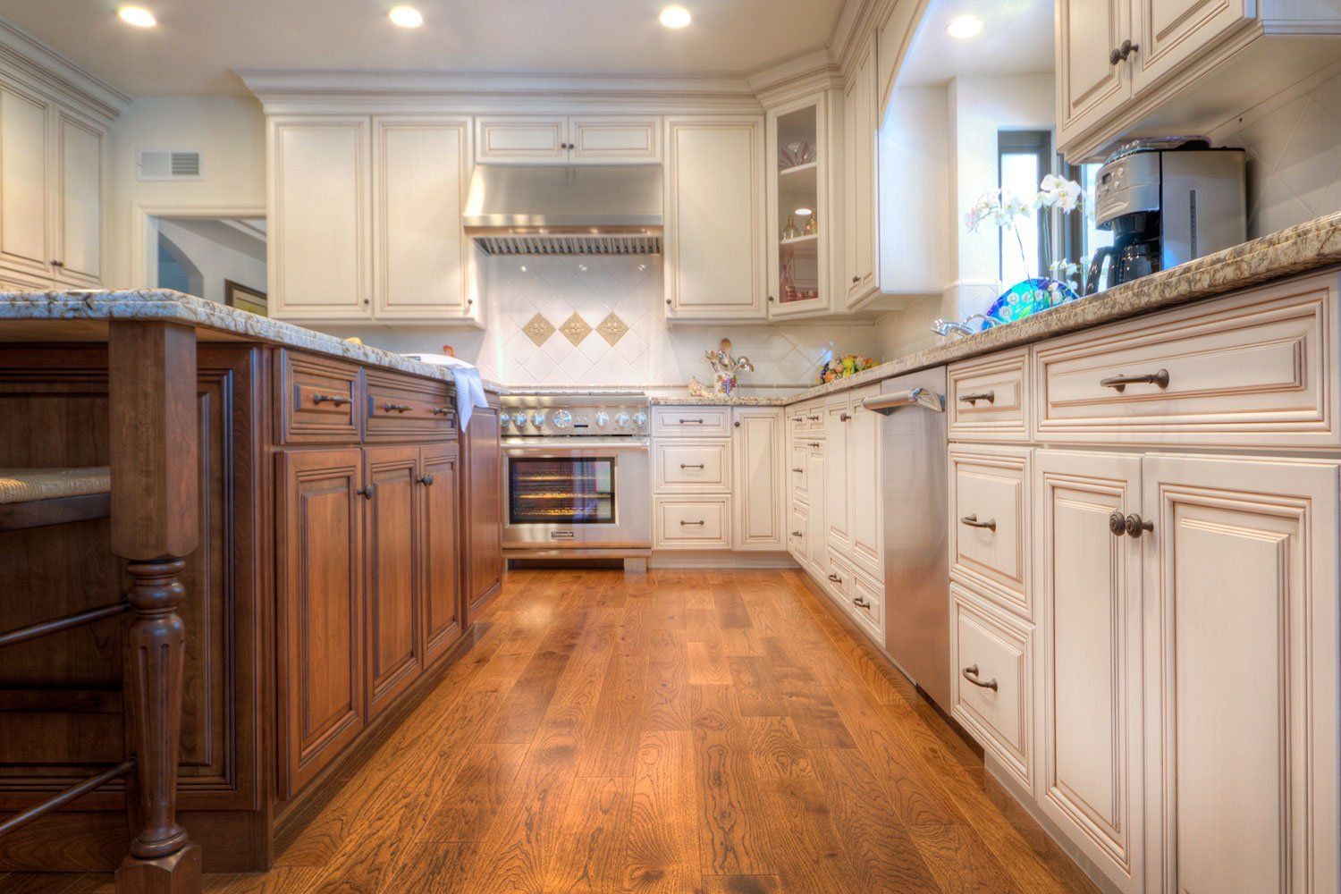 Bright kitchen with white cabinets, granite countertops, hardwood floor, and stainless steel stove and hood