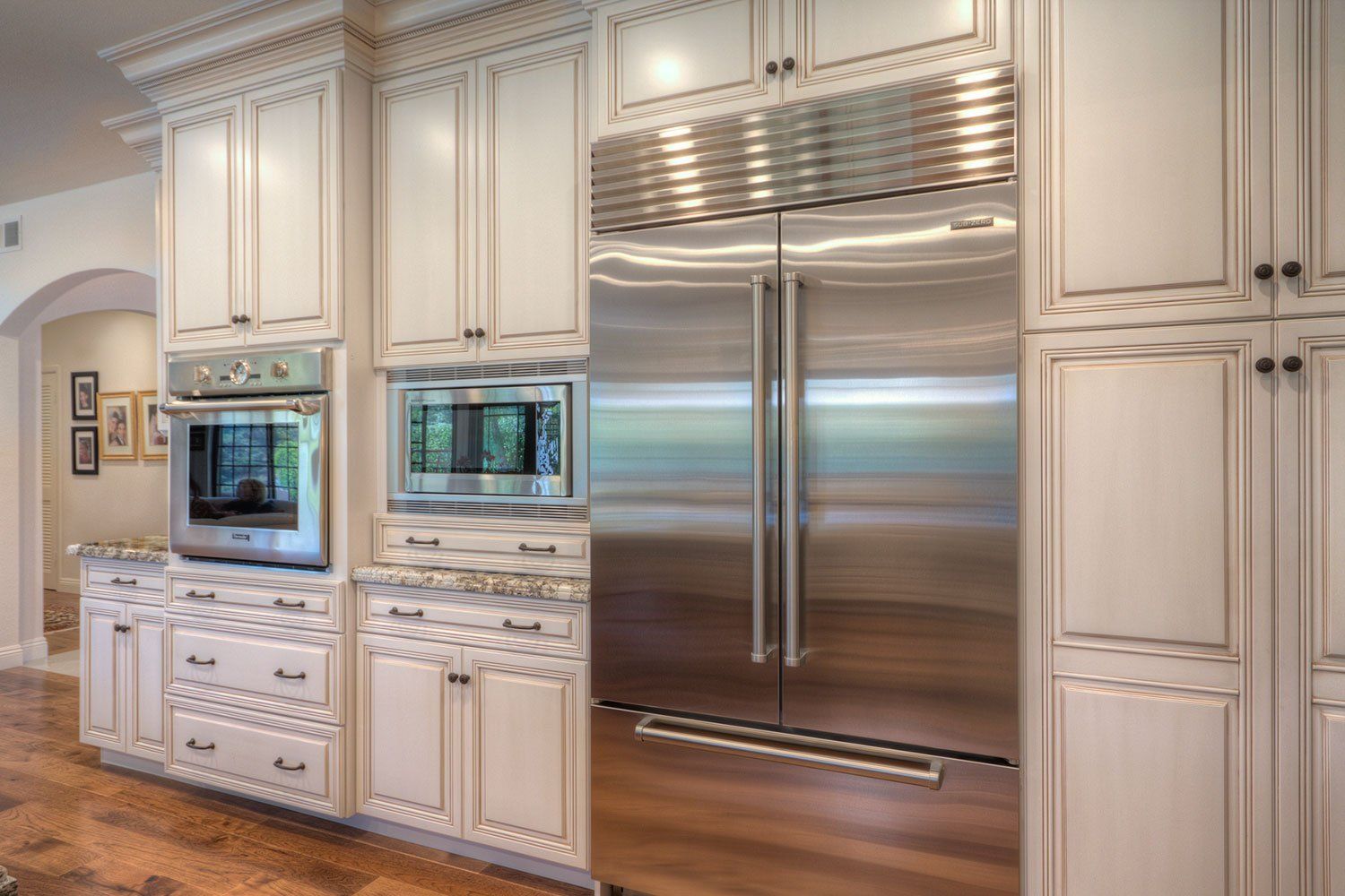 Elegant white kitchen with stainless steel double refrigerator, built-in ovens, and marble countertops