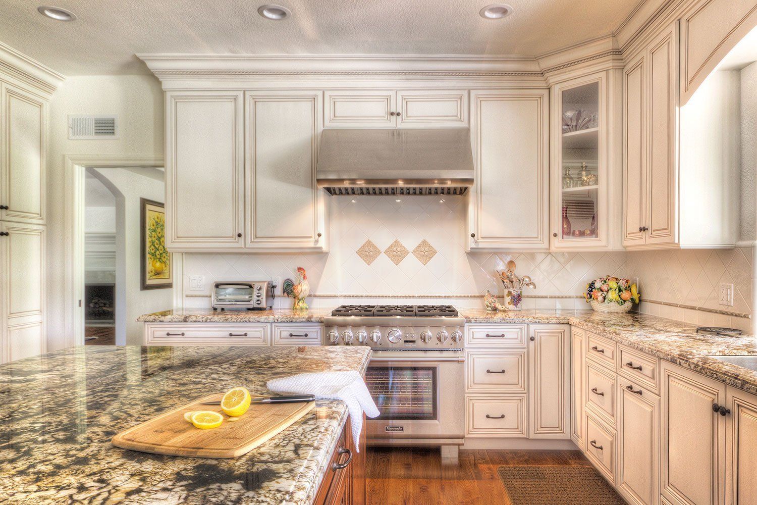 Bright white kitchen with granite island, stainless stove, cabinets, and lemon slice on a cutting board.