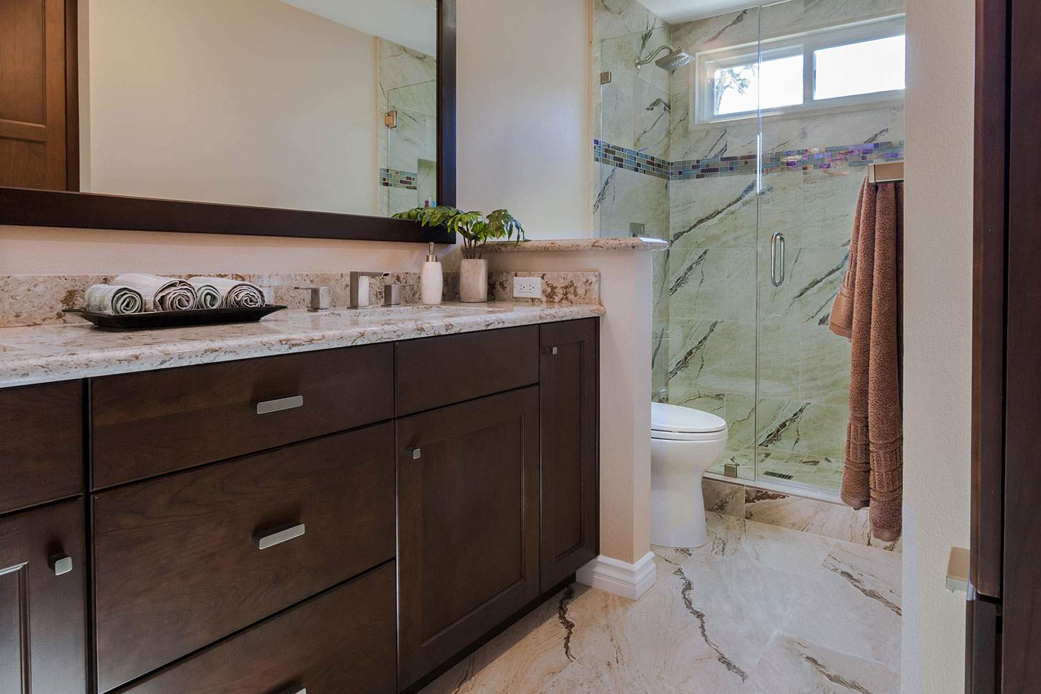 Modern bathroom with dark wood vanity, marble countertop, large mirror, and glass shower.