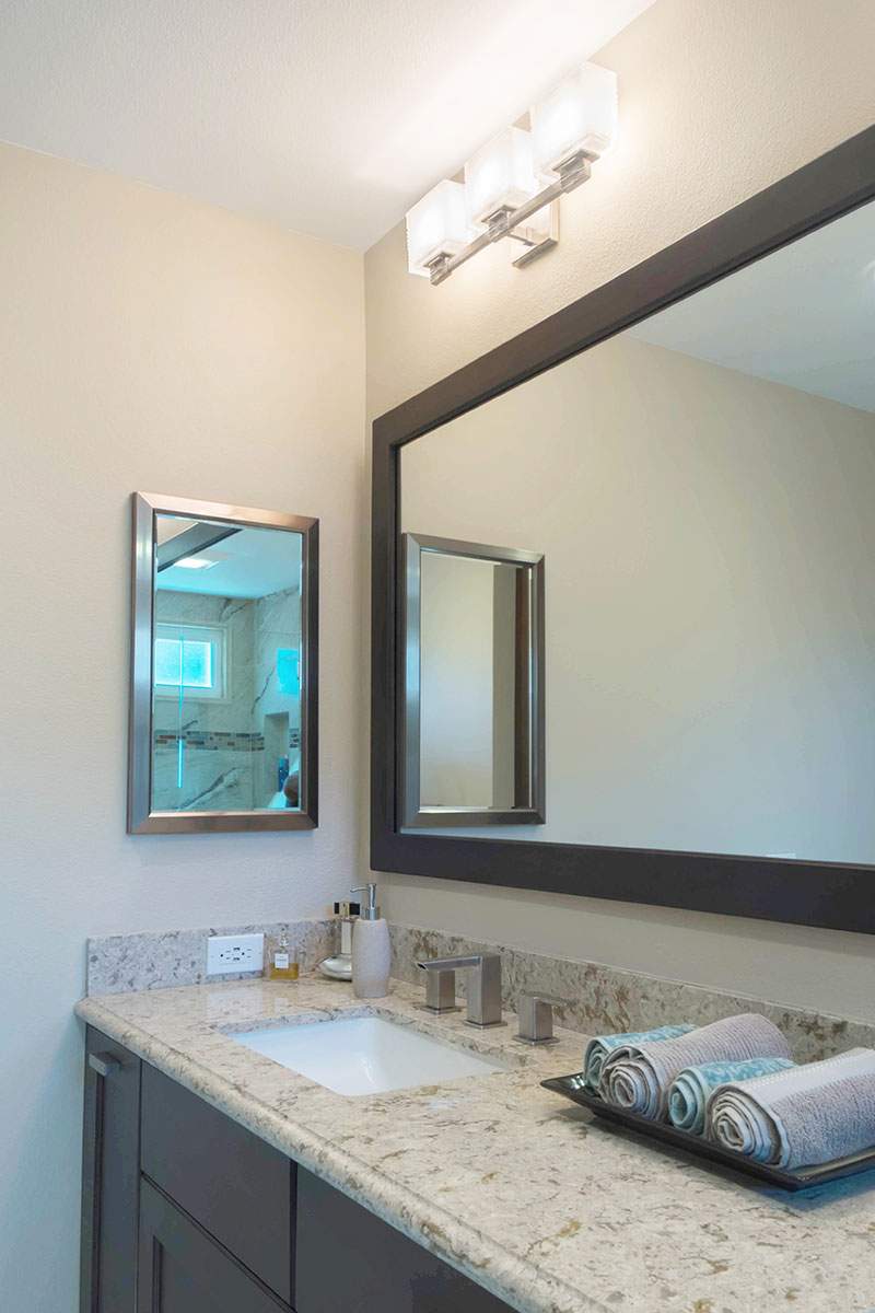 Bathroom vanity with granite countertop, large mirror, wall light, and folded towels