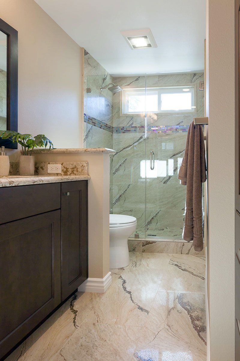Modern bathroom with marble tile, glass shower, vanity, and window light