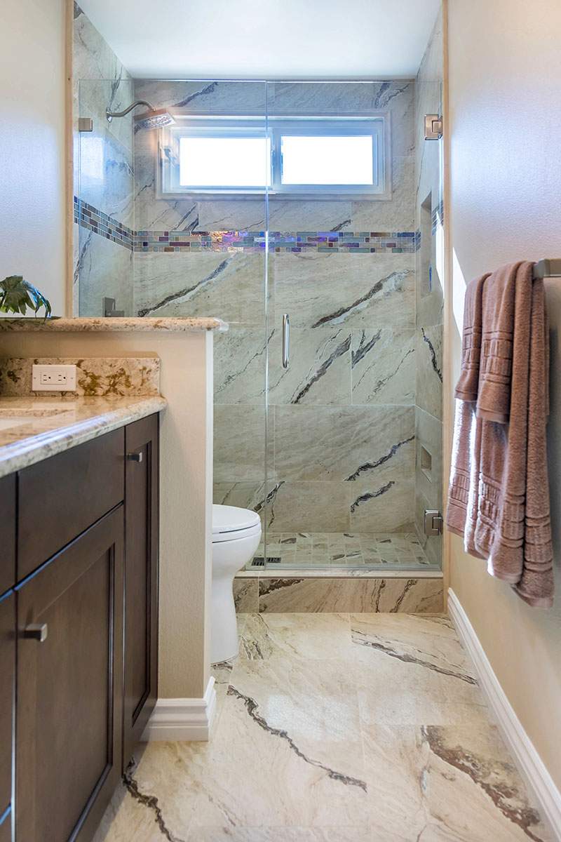 Narrow bathroom with marble tile shower, dark wood vanity, and towel hanging on the wall.