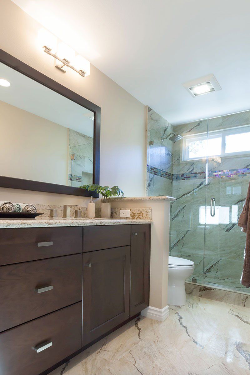 Modern bathroom with dark vanity, large mirror, white toilet, and green marble shower wall