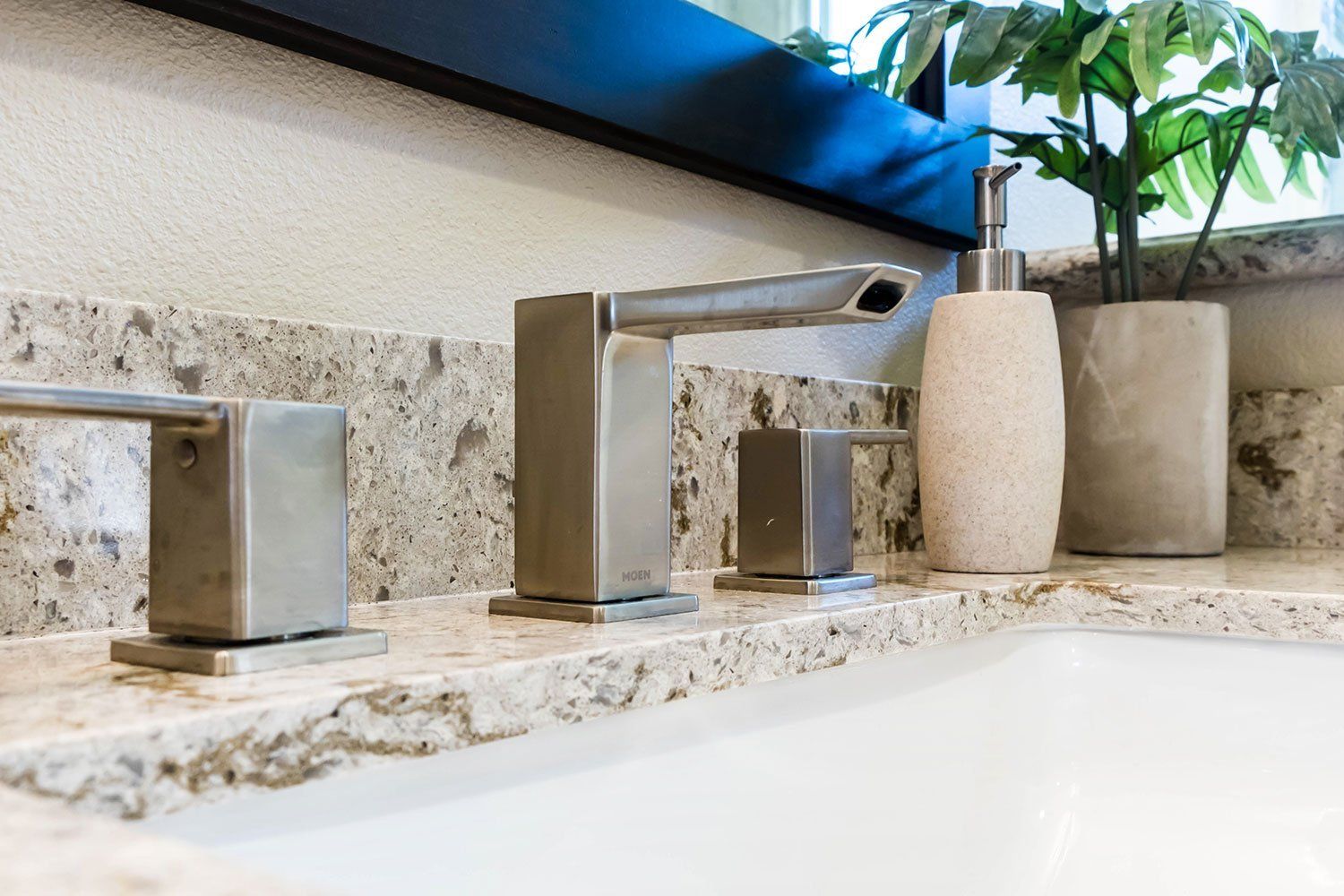 Modern bathroom sink with brushed metal faucet, white countertop, and potted plant decor