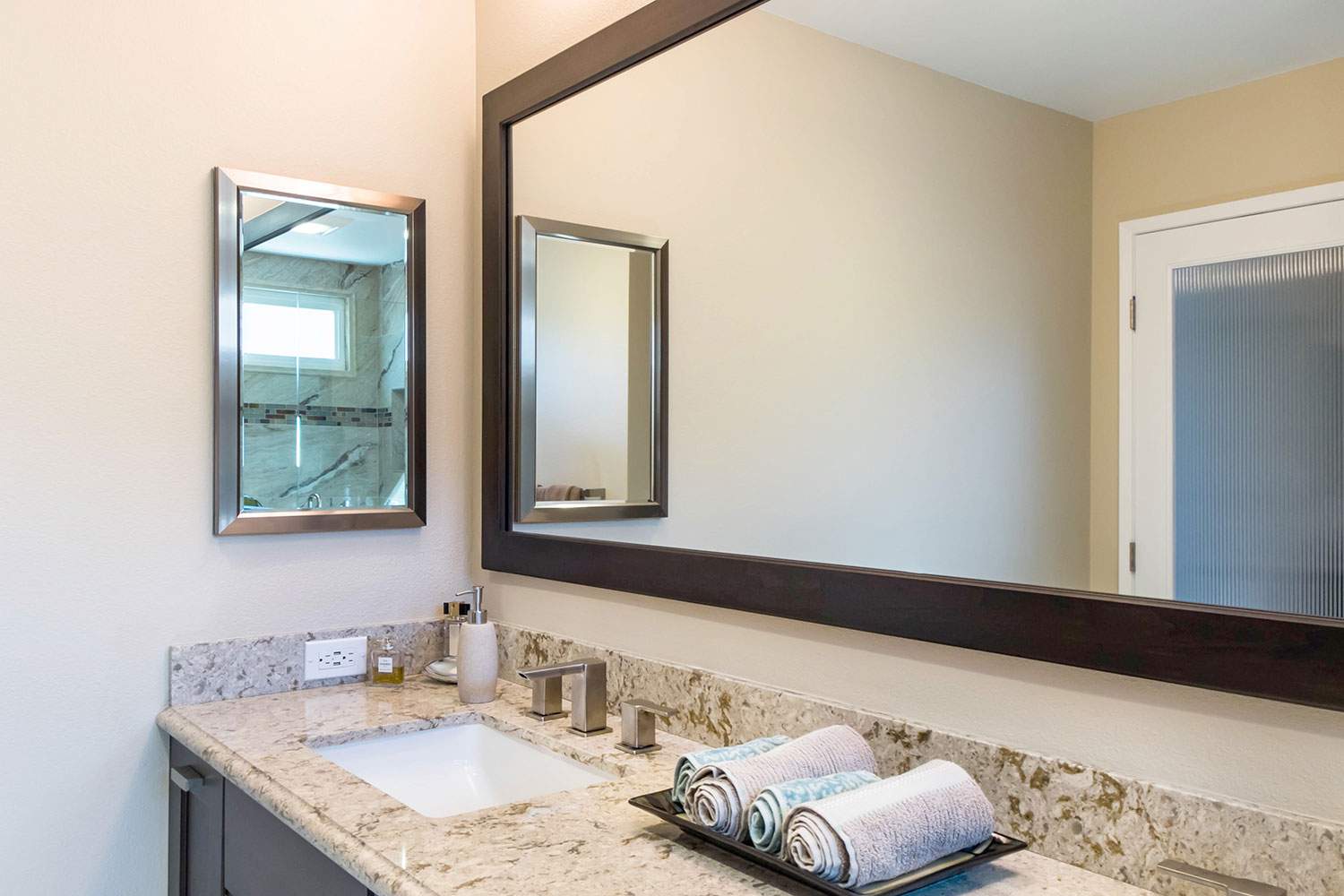 Bathroom vanity with granite countertop, sink, mirror, and folded towels on the counter