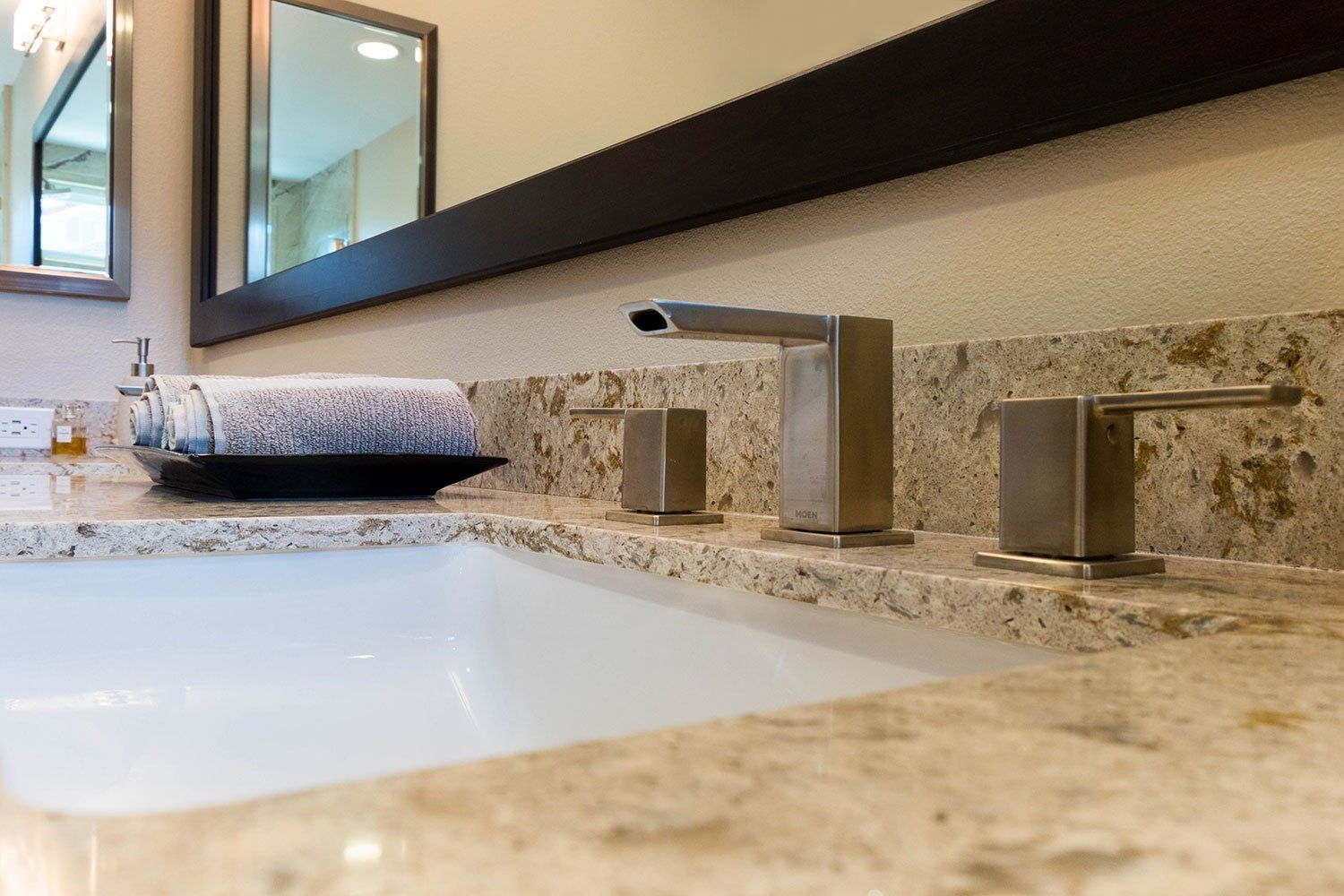 Bathroom sink with granite countertop, chrome faucet, mirror, and neatly folded towel.