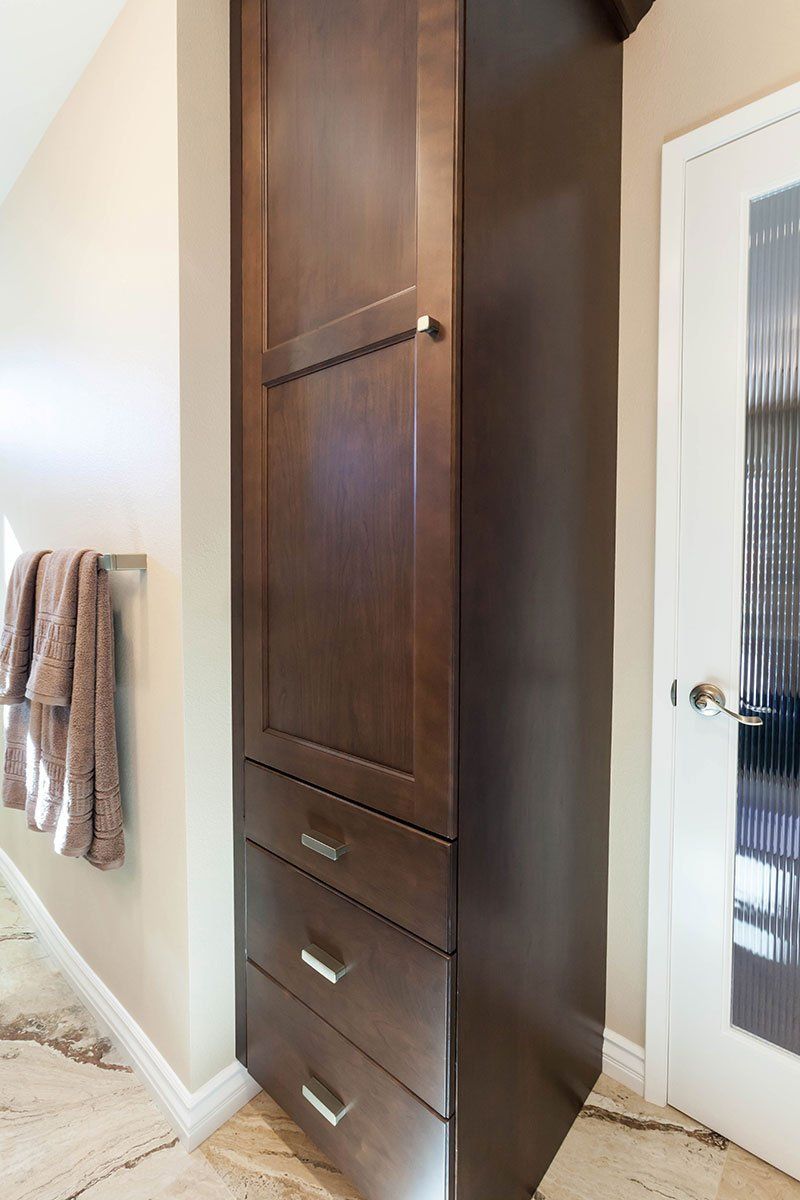 Tall dark wood storage cabinet beside a white door in a hallway or entryway.