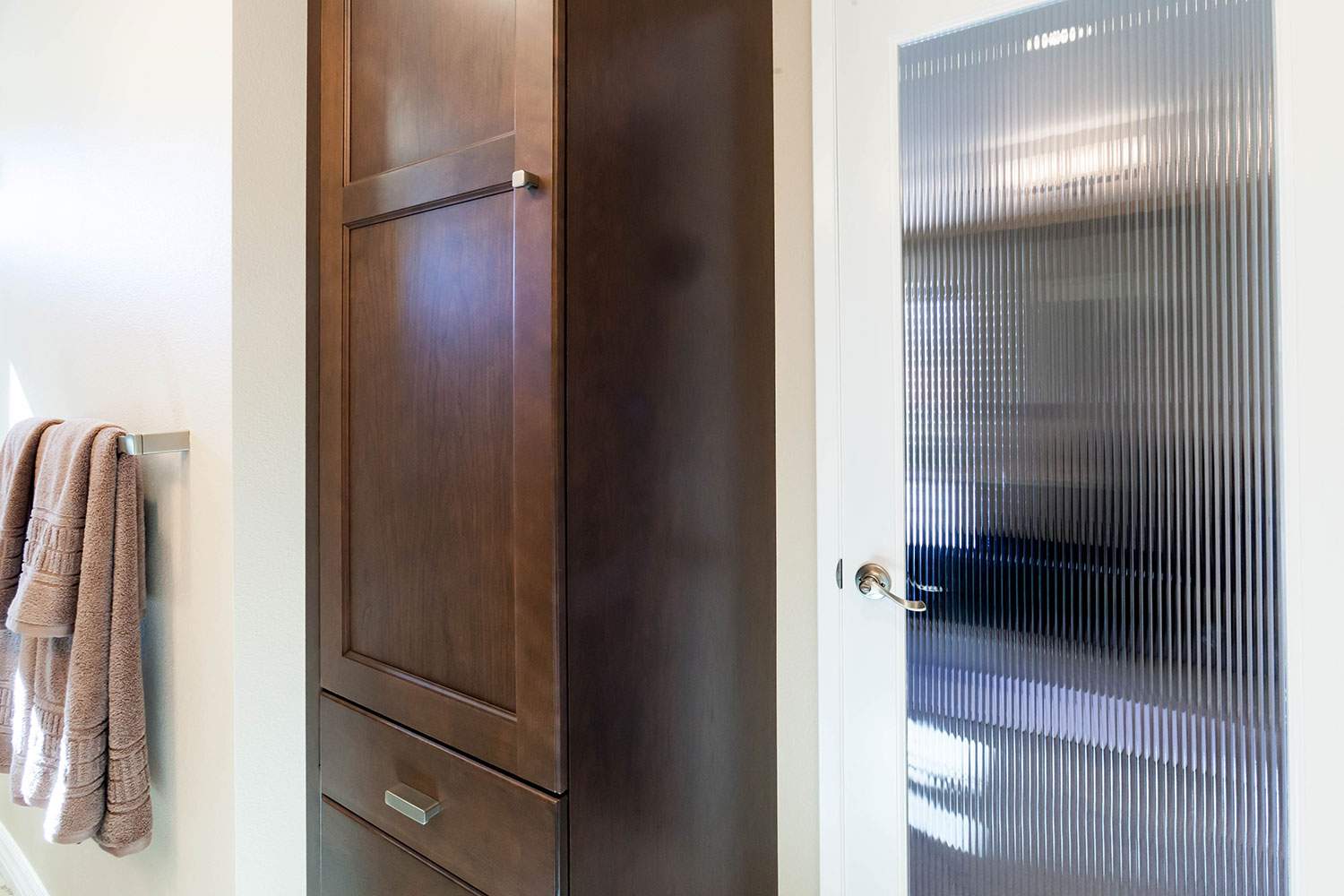 Bathroom wall with a wooden cabinet, towel, and frosted glass shower door