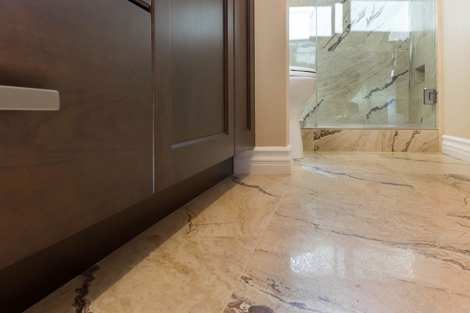 Marble bathroom floor with dark wood vanity and glass shower enclosure