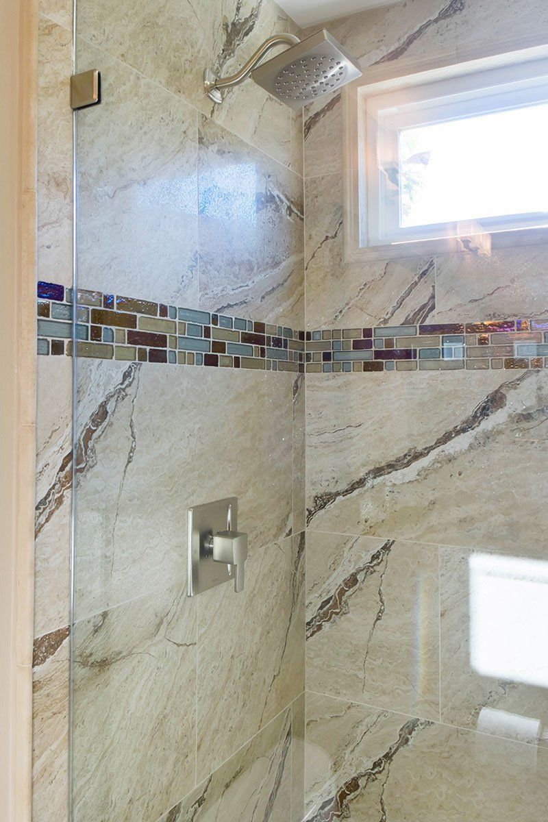 Marble-tiled shower with mosaic accent strip, chrome fixtures, and a small window.