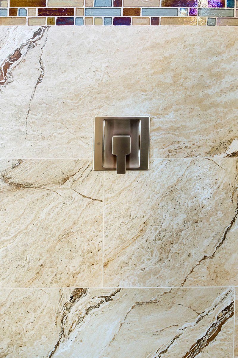 Silver wall-mounted bathroom faucet on beige marble tile wall