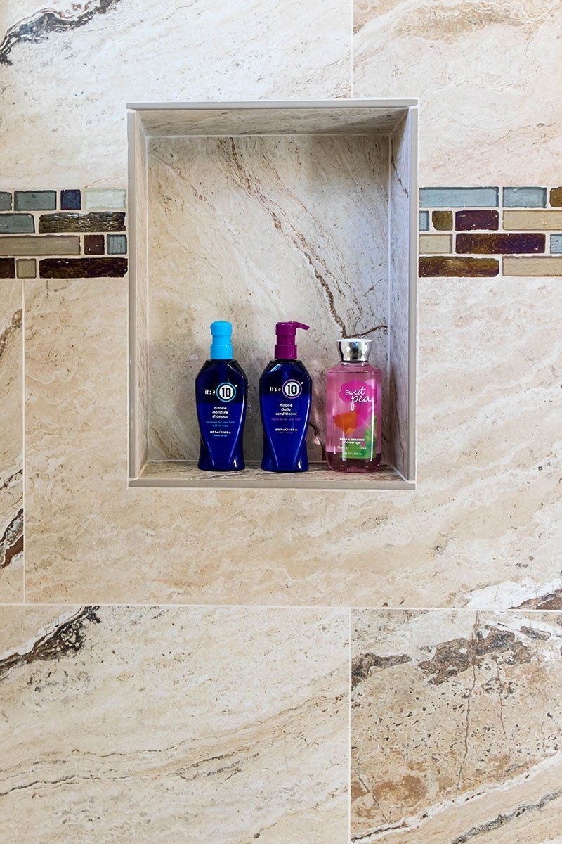 Bathroom shower niche with three bottles of toiletries on beige tiled wall