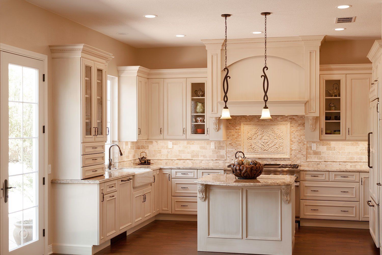 Bright cream kitchen with island, pendant lights, white cabinets, and stone backsplash