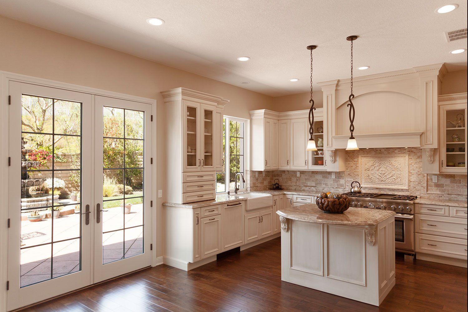 Bright modern kitchen with white cabinets, island, stone backsplash, and French doors to a patio