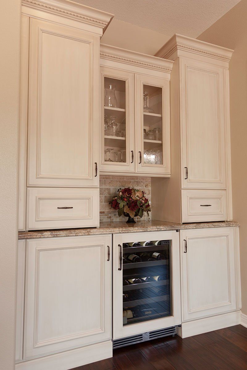 White kitchen cabinets with marble countertop and built-in wine cooler beneath glass-front upper cabinets