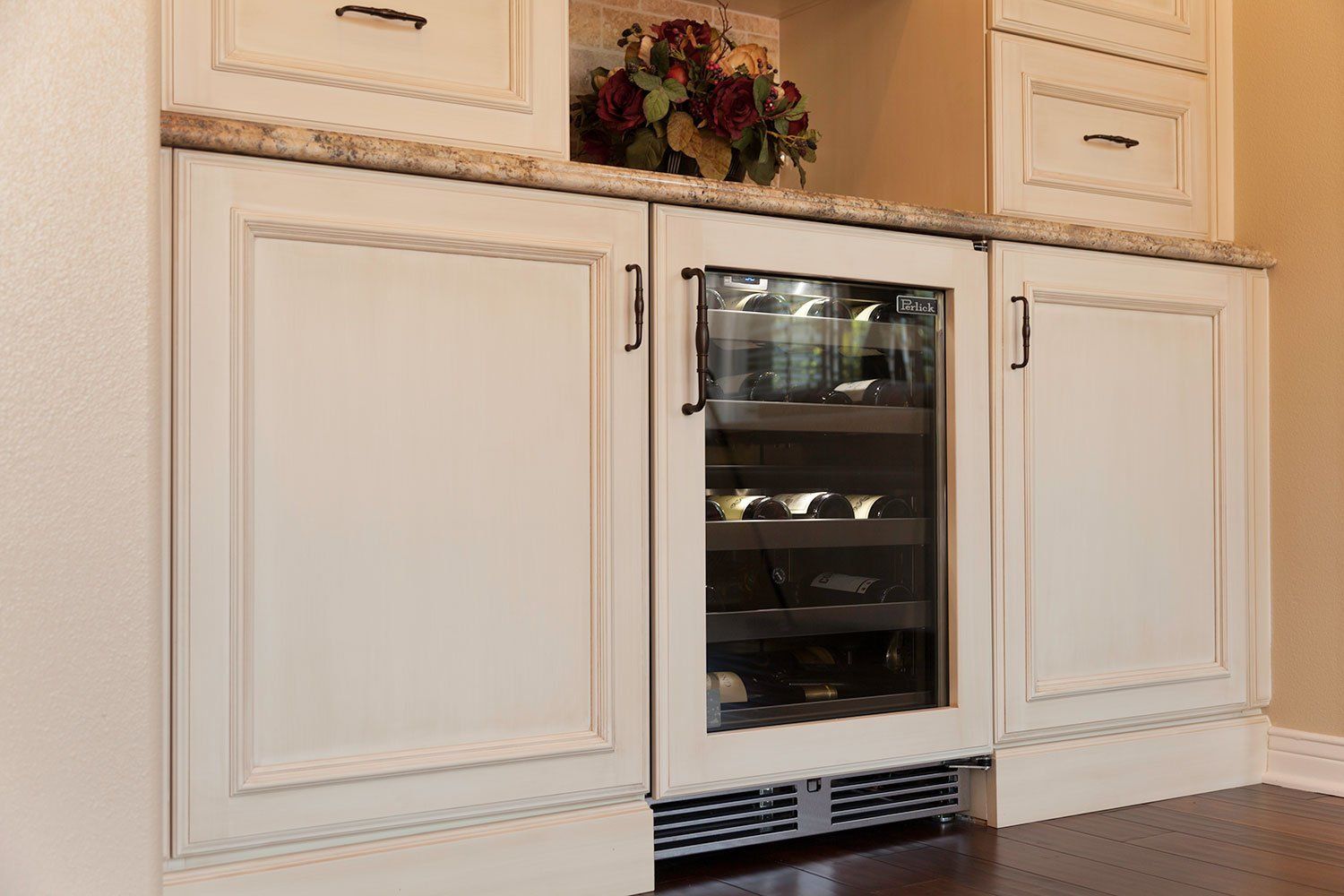 White kitchen cabinets with a built-in stainless steel wine cooler and decorative greenery above