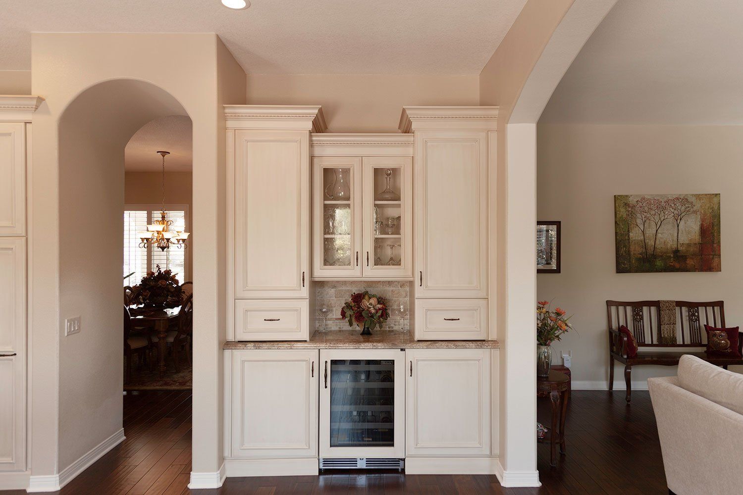 White built-in cabinet with glass doors in a beige living room and arched doorway