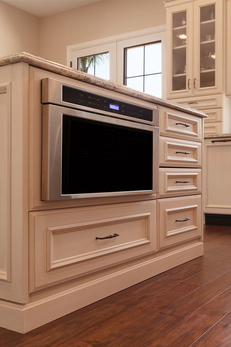 Built-in white kitchen oven and cabinetry with drawers and glass-front cabinet above on a wood floor