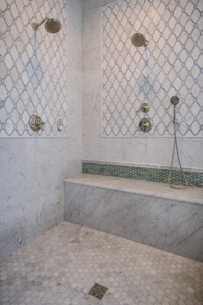 Small tiled shower area with a built-in bench, wall fixtures, and a floor drain