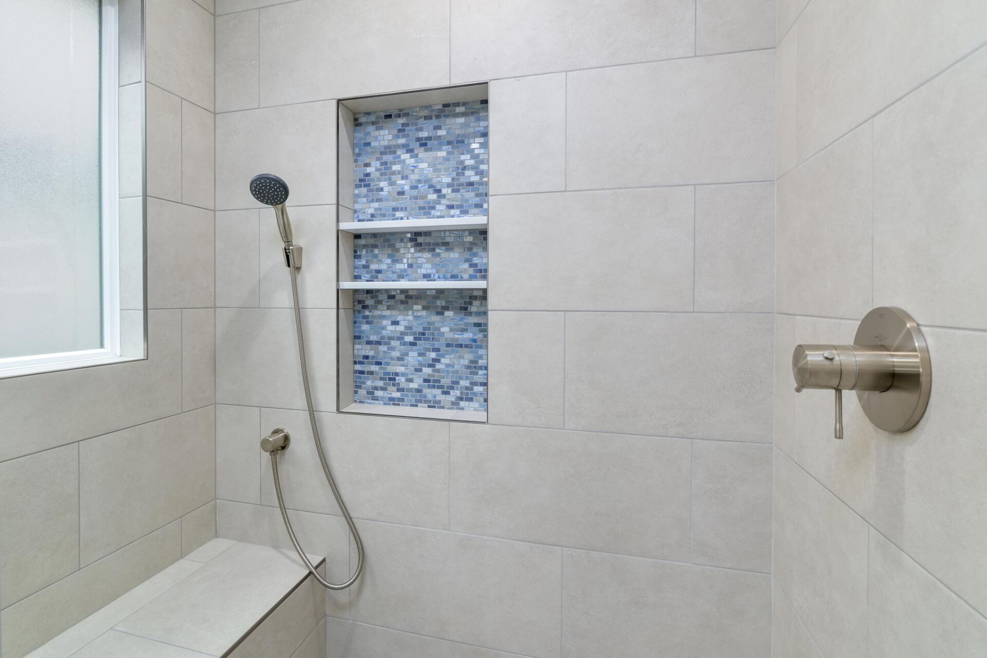 Tiled shower with handheld showerhead, frosted window, and wall-mounted grab bar