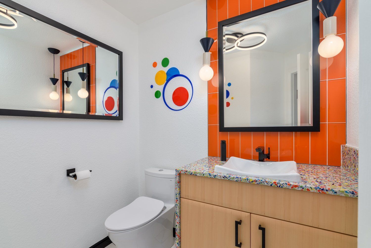 Modern bathroom with orange accents, large mirror, granite sink vanity, and white toilet