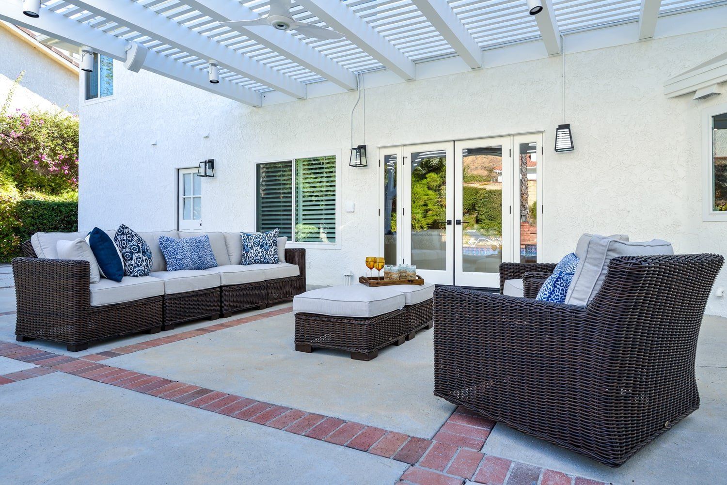 Patio with dark wicker sofa and chairs, blue cushions, and a coffee table under a white pergola.