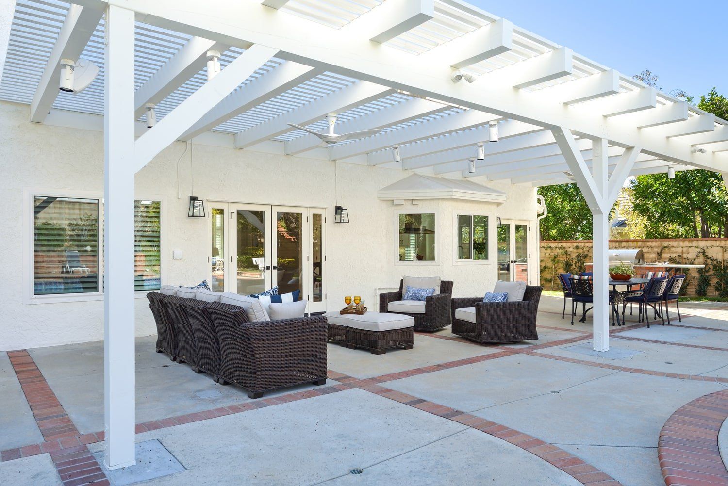 Outdoor patio with white pergola, wicker seating, and brick pavers beside a house